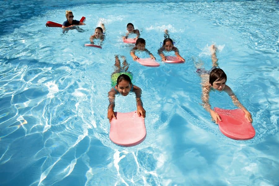 Children practicing swimming with kickboards in a pool